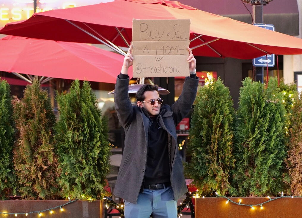 buy or sell a home Ash holding a sign that reads buy or sell a home with Ash Arora